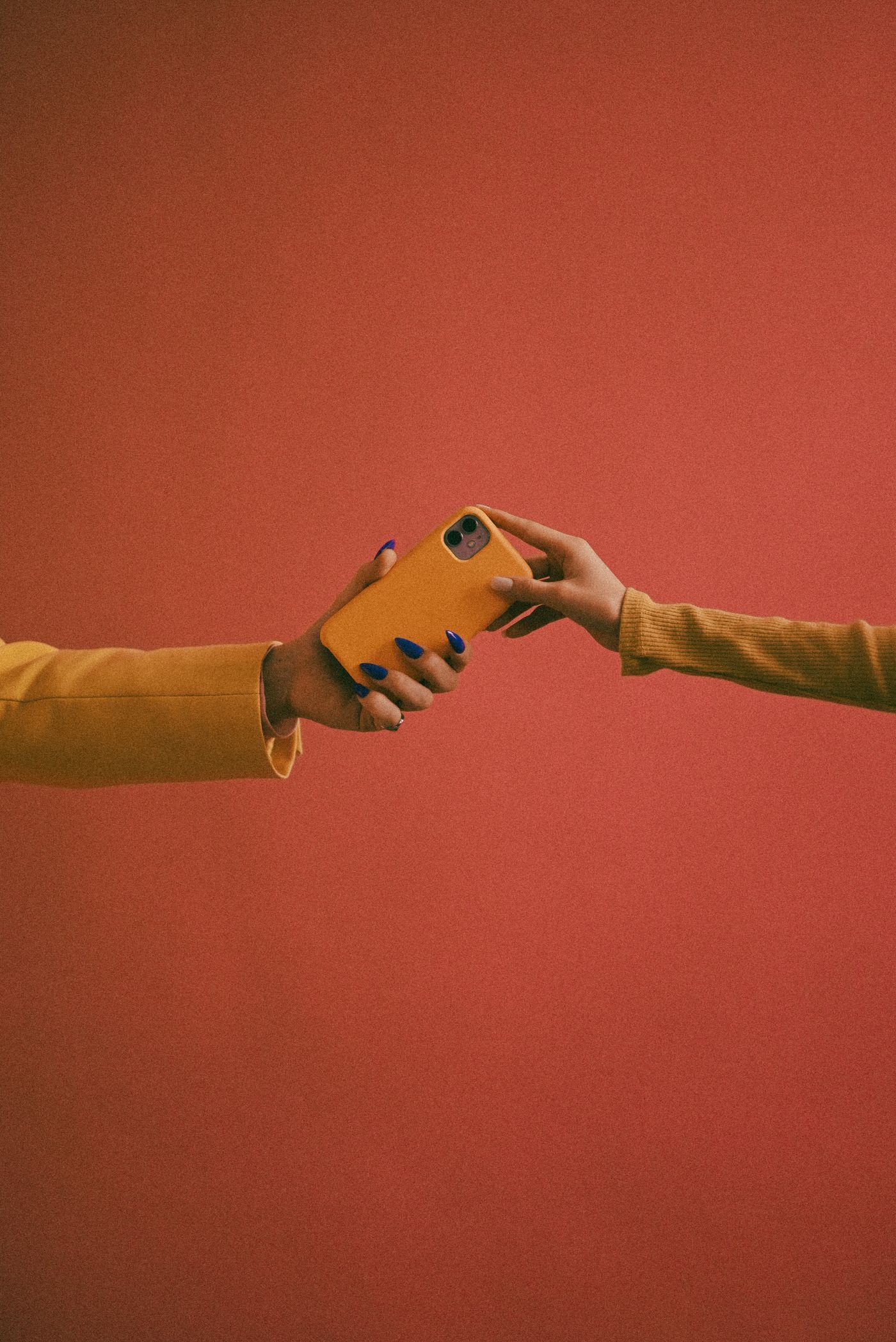 Dos manos se pasan un celular amarillo sobre un fondo rojo